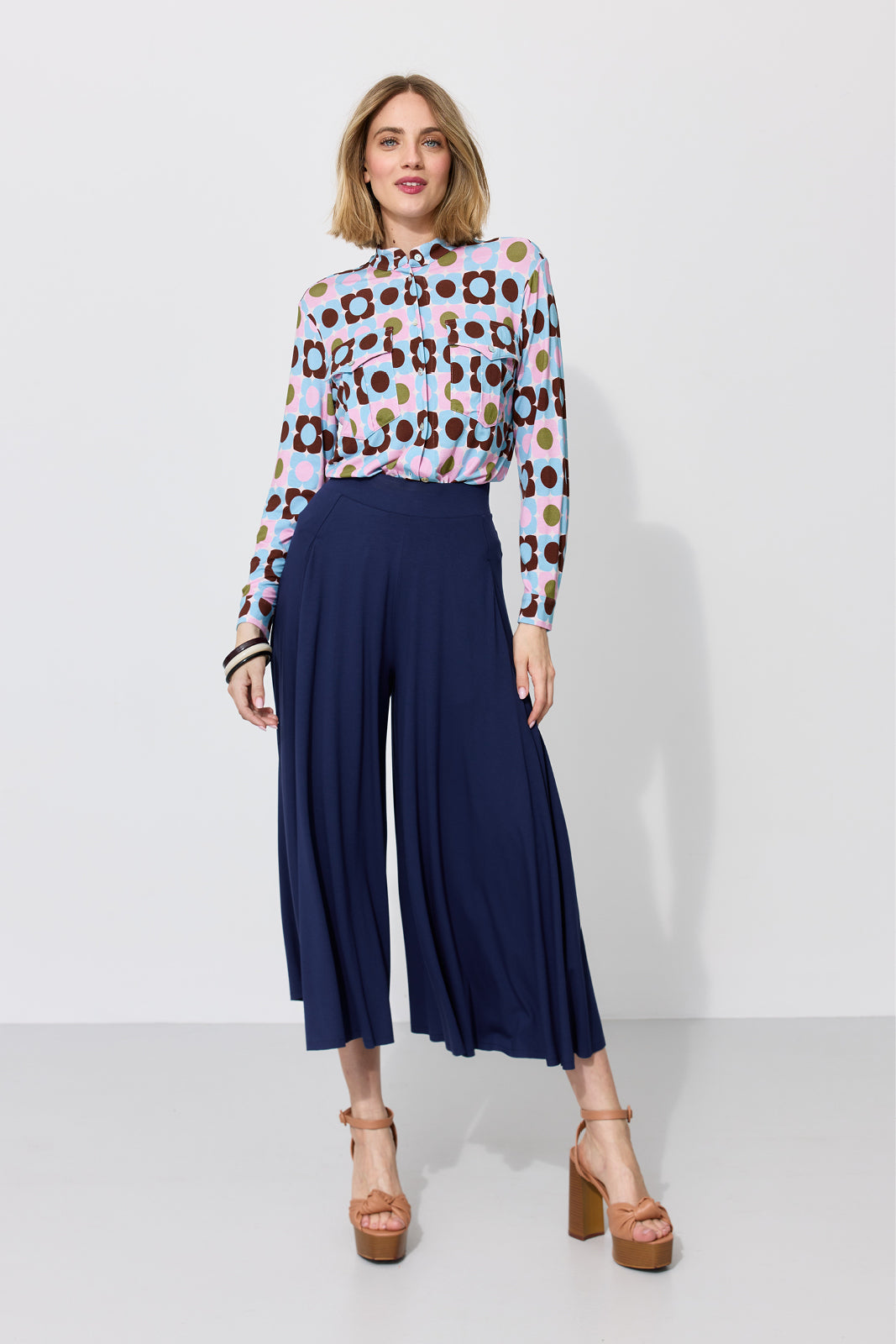 Kobieta w kolorowej bluzce z kwiatowym wzorem i granatowych spodniach culottes, stylowa moda damska