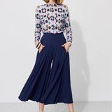 Kobieta w kolorowej bluzce z geometrycznym wzorem i granatowych spodniach culottes, stylowa moda damska