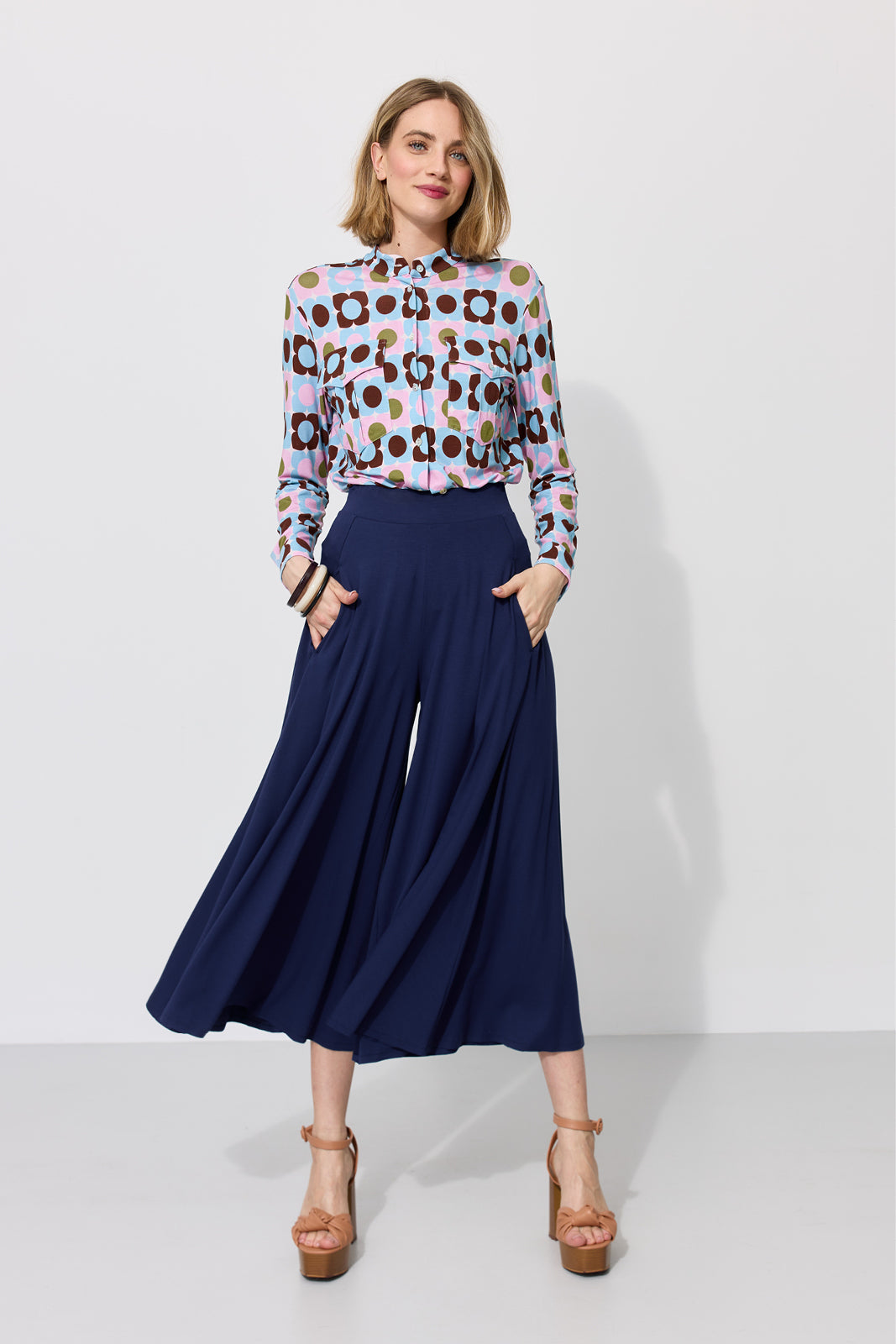 Kobieta w kolorowej bluzce z geometrycznym wzorem i granatowych spodniach culottes, stylowa moda damska