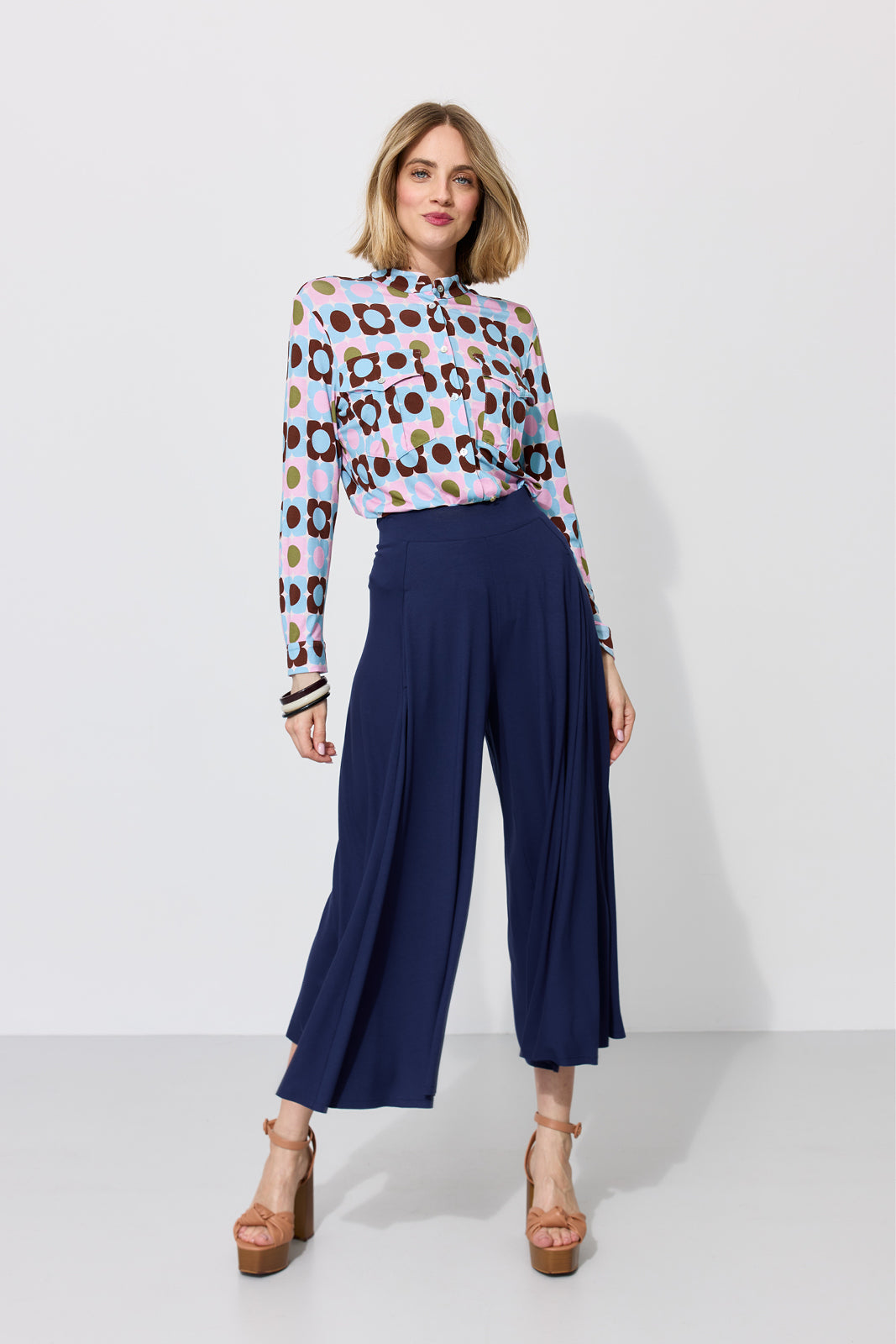 Kobieta w kolorowej bluzce z kwiatowym wzorem i granatowych spodniach culottes, stylowa moda damska