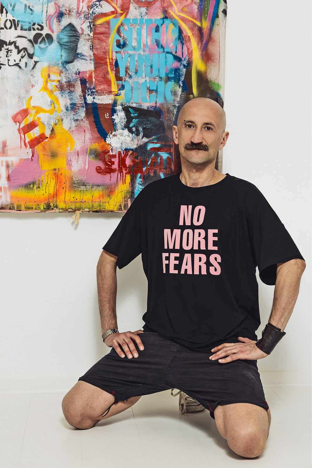 Mężczyzna w czarnej koszulce z napisem 'NO MORE FEARS' przed kolorowym graffiti, styl uliczny, moda z kulturą