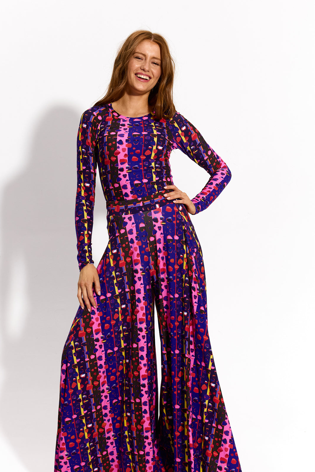 Kobieta w kolorowej, graficznej sukience z długim rękawem i szerokimi nogawkami, stylowa i wygodna, idealna na codzień